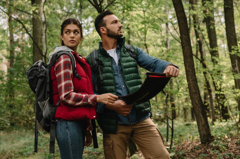 Man and woman looking for destination on map while hiking in forest together.